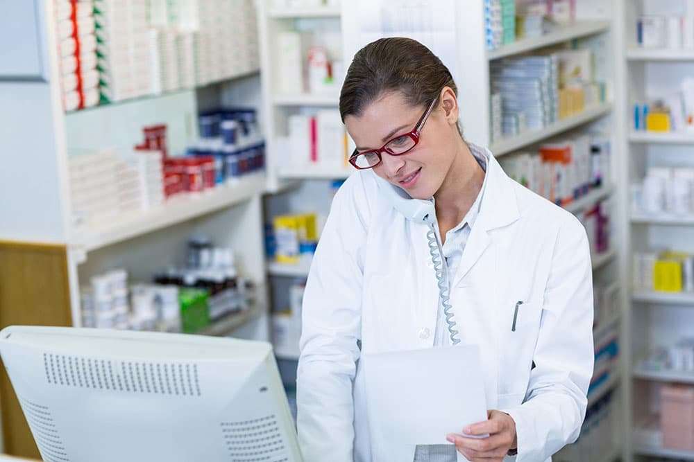 A CEO's Guide to Hospital Marketing (Digital) 6 Pharmacist holding prescription paper while talking on phone in pharmacy